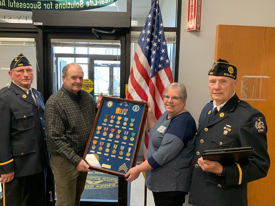 Denny Hansen and Doug Thompson flank John Hatcher and Margo Davis, Center Operations Supervisor, USO Rock Island Center as they hold a shadowbox containing medals earned by Eugene Parker, a Navy and Air Force veteran buried in the Rock Island National Cemetery at the Rock Island Arsenal.