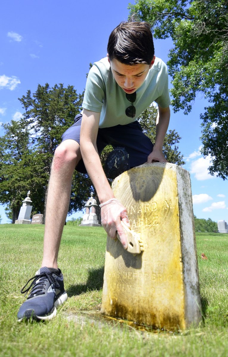 Aaron Schultz uses a soft brush to scrub the gravestone of Leonard Stahle in the Oakland Cemetery west of Solon. Schultz has been volunteering his time to clean veterans&#8217; graves and uses the same materials and techniques as are used in national cemeteries.