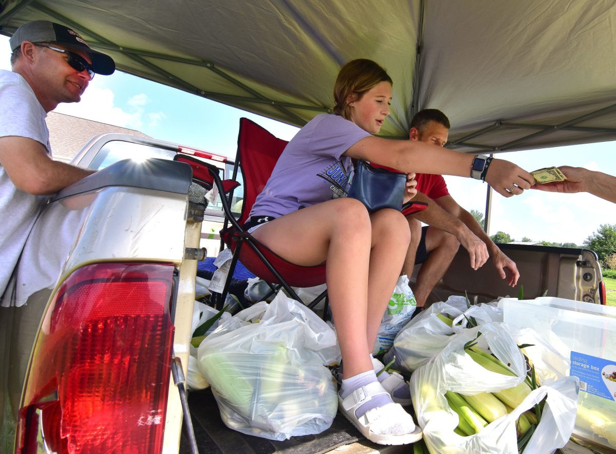 Audrey takes payment for a dozen ears of locally grown sweet corn as Kyle Stahle (at left) looks on. Kyle, his family, and friends grew sweet corn for the first time this year after Dean Rebel announced he wouldn&#8217;t be planting any this season. They&#8217;ve been selling the corn for a few weeks now in front of the Dairy Queen.