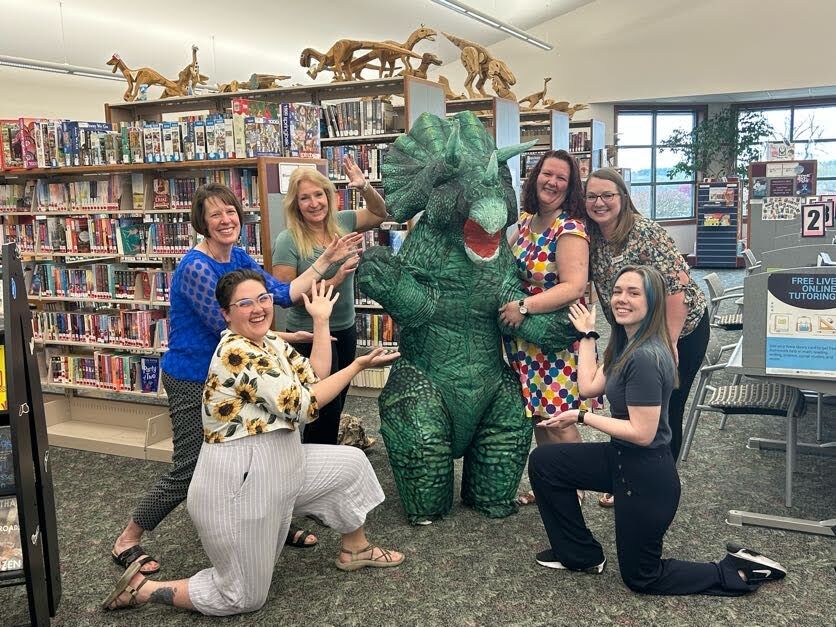 (From left) Lilly Smith (Youth Services Librarian), Liz King (Library Director), Sherri Chalupa (Cataloging Librarian), Trixie (Dinosaur-in-Residence), Alexis Kurth (Adult Services Librarian), Megan Richardson (Communications Specialist), and Madison (Teen Services Librarian)