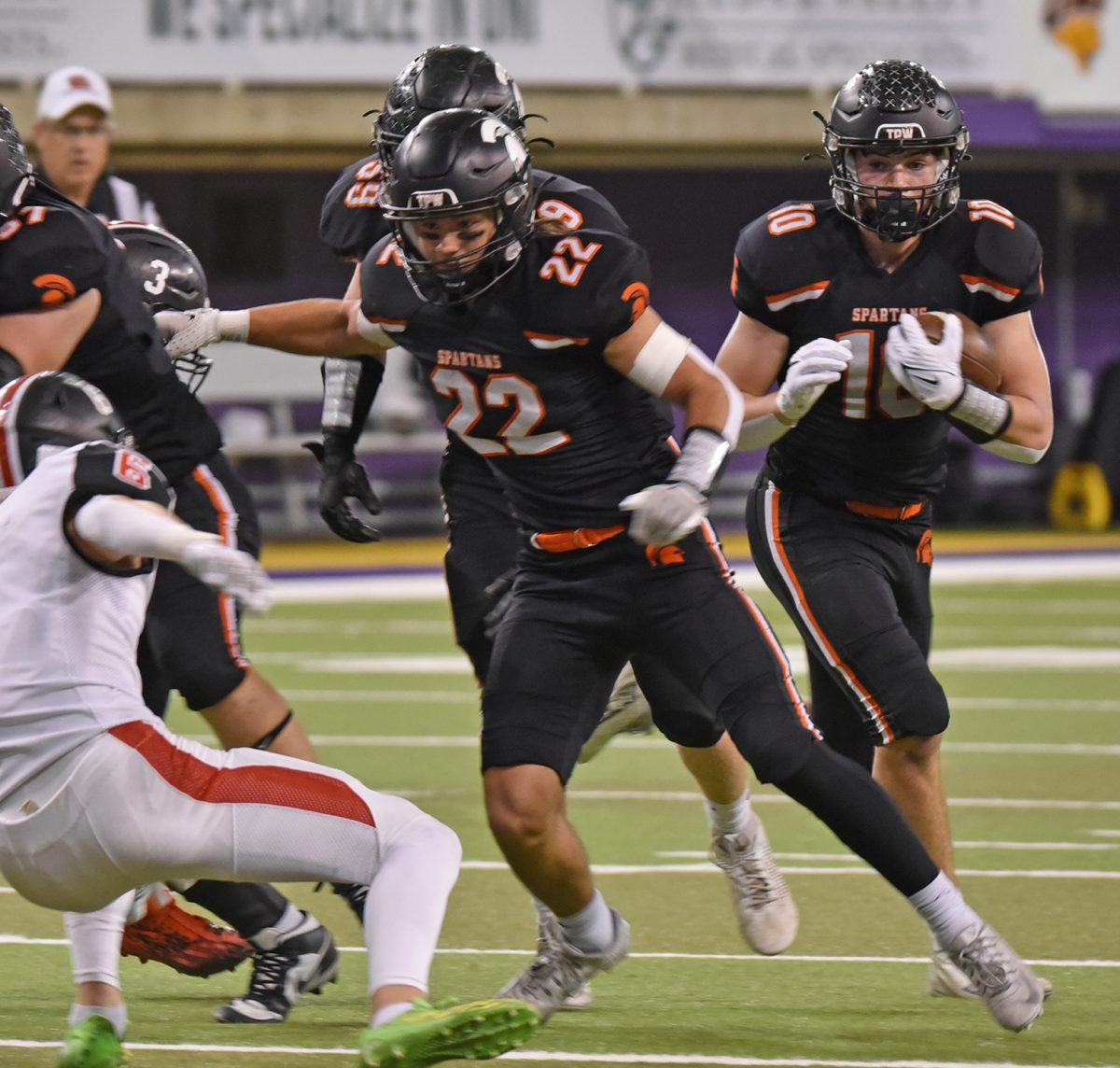 Trevor Myers (57), Conlan Poynton (22), and Mason Scott (59) work to clear a path for Eddie Johnson (10) in a Class 3A State Semifinal game this past Saturday against Williamsburg in the UNI Dome in Cedar Falls.