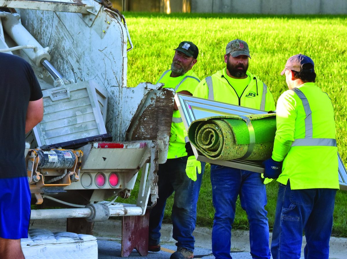 Two employees of Johnson County Refuse wait while a third crushes and compacts a plastic deck box during the annual Citywide Clean Up Day this past Saturday morning at the SRNA. Residents were able to dispose of unwanted items cluttering up their property during the two-hour event.