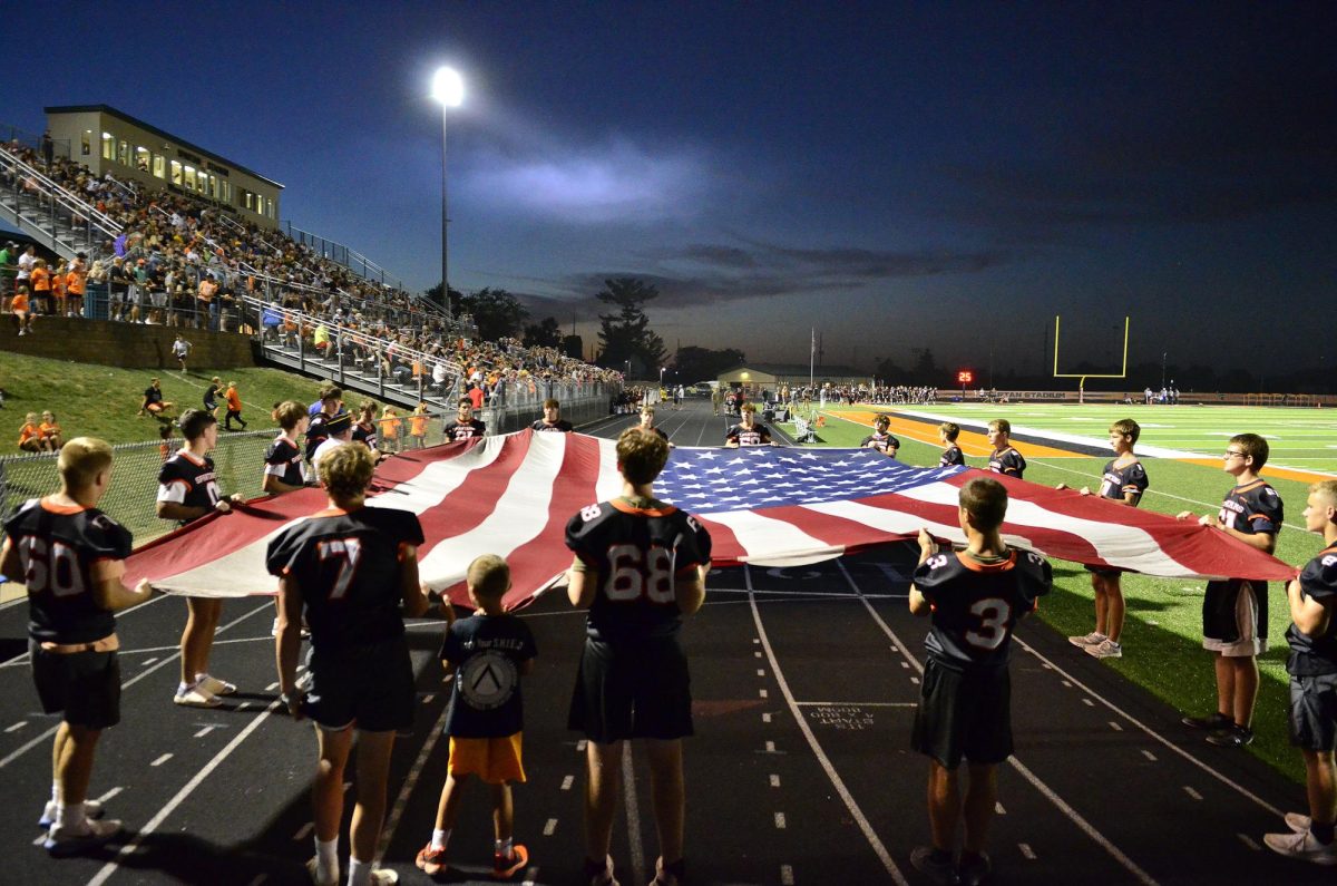 The sophomore football team carries a 35’ American Flag (on loan from the Cedar Rapids Fire Department) along the sideline as pregame ceremonies for Armed Forces Night are about to get underway this past Friday during the Mount Vernon vs. Solon varsity football game.