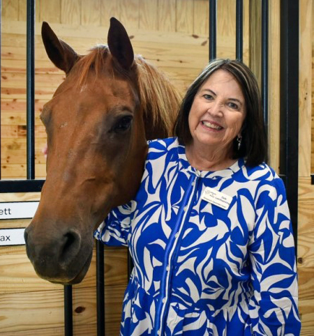 Executive Director of Miracles in Motion Deb Leichsenring poses with a horse poking its head out of a wooden stall.
