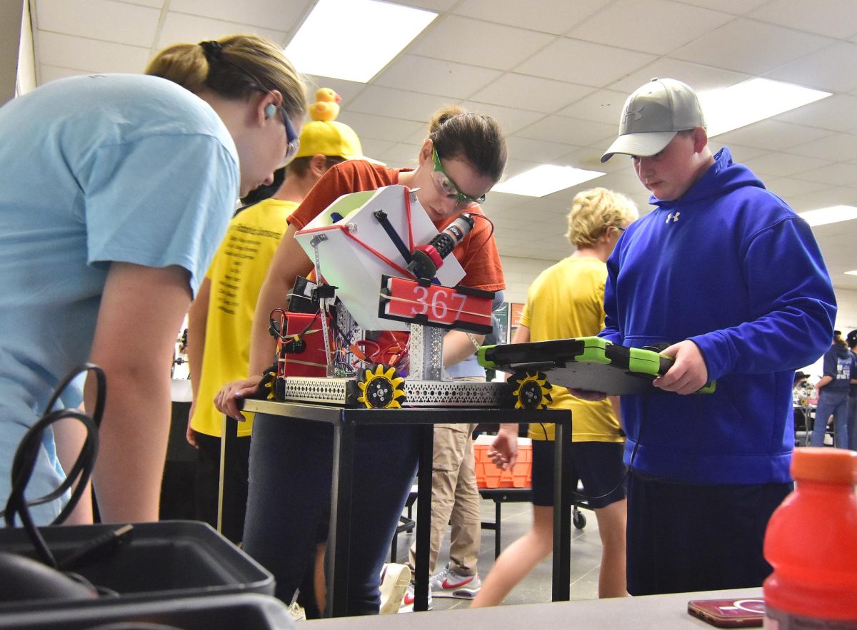 Volunteer and mentor Sammy Edwards (middle) pre-inspects Solon Robotics Team 367, “Organized Chaos’” robot before a scrimmage match Thursday, October 16 at the Solon Community Center. Edwards, in her mid-20s, has been involved in robotics at all levels since she was in middle school and helps start new robotics clubs while assisting Solon’s program.