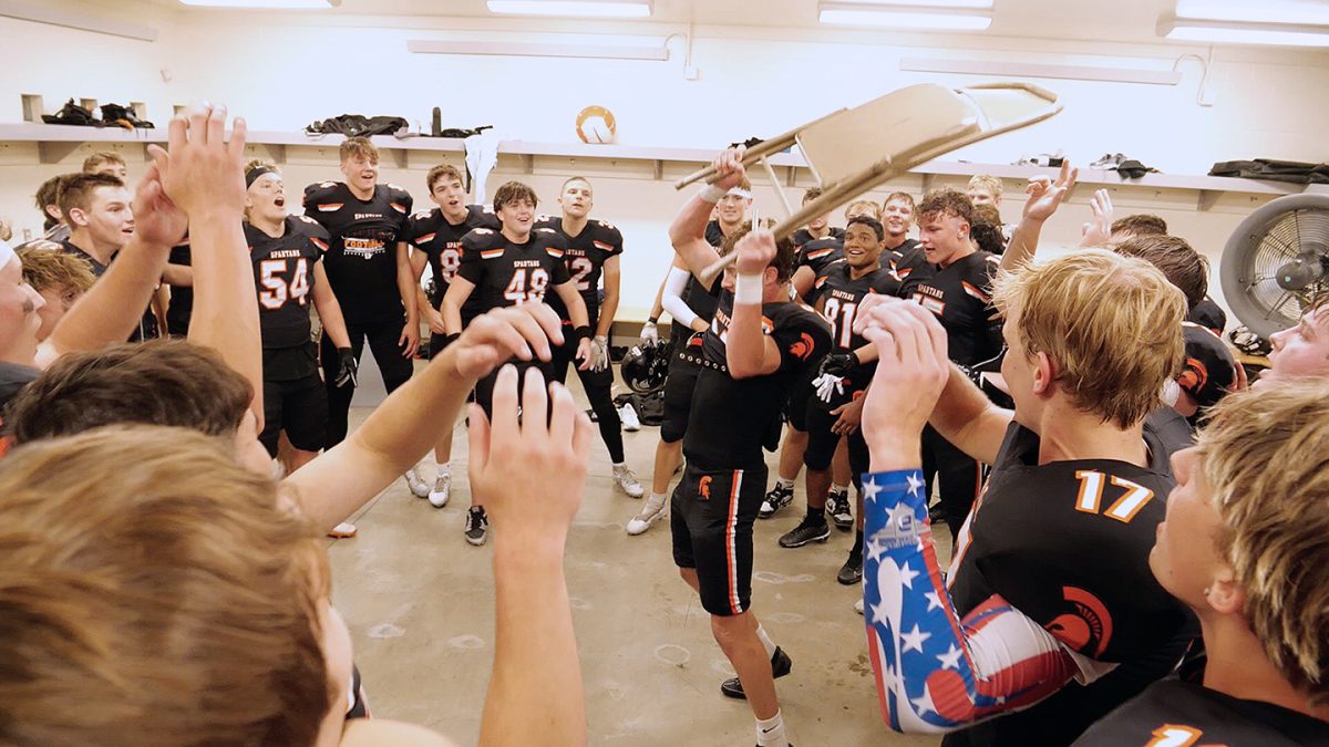 Owen Bock prepares to slam a metal folding chair against the locker room floor after a recent win. Bock, a sophomore, had made a touchdown, earning the right to pummel the chair in what has become a Spartan tradition.
