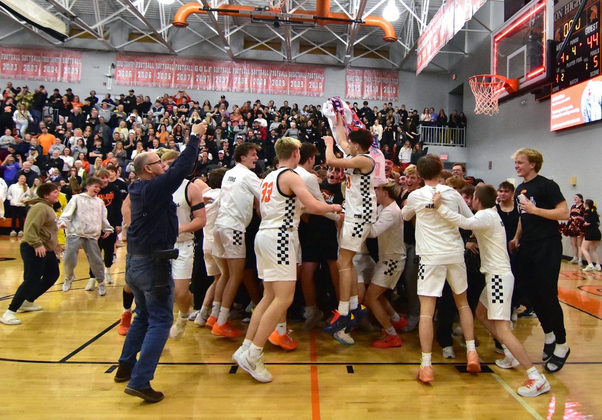 Tate McCollum jumps up and down with the Class 3A State Basketball Tournament Qualifier banner in a celebratory scrum with his teammates after getting past the Central DeWitt Sabers 49-44 Monday.