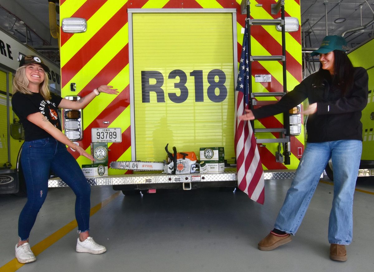 Big Grove Brewery’s Dacey Johnson, Marketing & Event Manager at Big Grove Brewery (at left) and Katie Neuzil, Store Director, Big Grove Solon, provide a little flair as they introduce Big Grove’s newest brew, Neighborhood Beer, and the chainsaw the Solon Fire Dept. was able to purchase as the first recipient of a $1k donation by Big Grove through their Neighborhood Beer Micro-Grant Program. Proceeds from every case sold will be reinvested into the Big Grove for Good Foundation, providing grants for community organizations and projects.